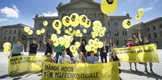 Das Bild zeigt mehrere Personen mit gelben Luftballons und einem Banner, "Hände hoch für Waffenkontrolle"