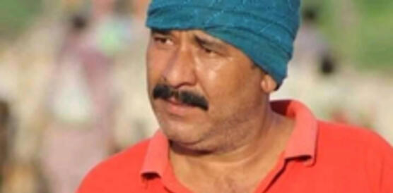 Ein Mann trägt ein rotes T-shirt und einen blauen Turban um den Kopf gewickelt.