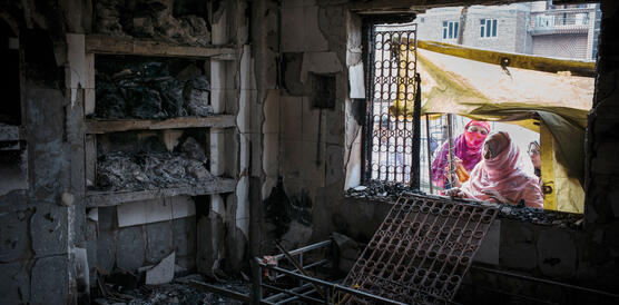 Indische Frauen mit Kopftüchern schauen durch ein Fenster ins Innere eines ausgebrannten Raumes.