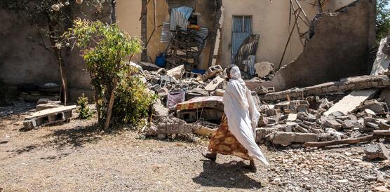 Das Bild zeigt im Vordergrund eine Frau, die an einem total zerstörten Gebäude vorbeiläuft