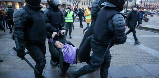 Das Bild zeigt Polizisten in schwerer Ausrüstung, wie sie eine Personen an Händen und Füßen davontragen.