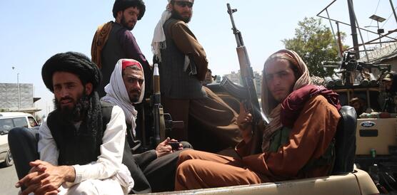 Das Bild zeigt schwer bewaffnete Männer mit Kopftüchern und Gewehren, sie sitzen auf der Ladefläche eines Autos