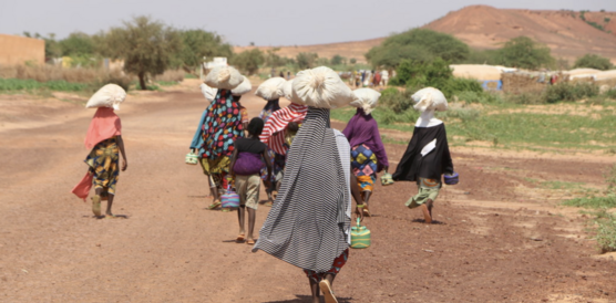 Das Bild zeigt mehrere Frauen von hinten, wie sie auf den Köpfen Säcke mit Proviant transportieren