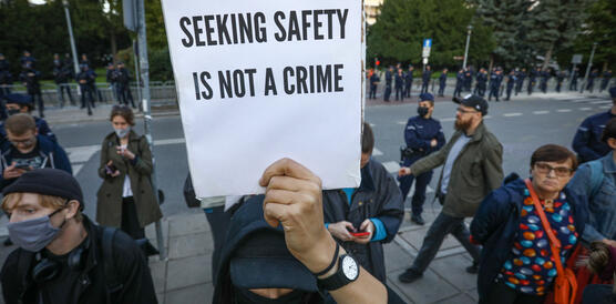 Das Bild zeigt eine Demonstration, in der Bildmitte ein Schild mit der Aufschrift "Seeking Safety is not a crime"
