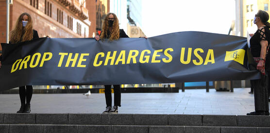 Das Bild zeigt Protestierende mit einem Plakat: "USA drop the charges"