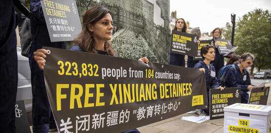 Das Bild zeigt mehrere Menschen, die mit Plakaten demonstrieren, darauf zu lessen "Free Xinjiang Detainees"