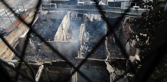 Das Bild zeigt die Überreste eines Hauses, das abgebrannt ist, das Mauerwerk. Rauch ist zu sehen.