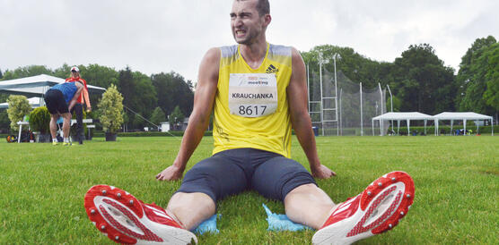 Ein junger Sportler in Läuferkleidung sitzt auf einem Rasen und beißt mit seinen Zähnen aufeinander.