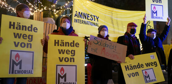 Das Foto zeigt mehrere Masken tragende Personen, die neben einem Amnesty-Banner mehrere Plakate mit der Aufschrift "Hände weg von Memorial" halten.