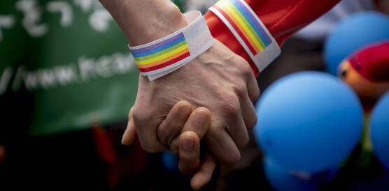 Das Bild zeigt zwei Hände mit Regenbogen-Armband