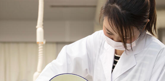 Eine Wissenschaftlerin in einem Kittel steht in einem Labor und schüttet eine Flüssigkeit von eibnem Gefäß in ein anderes.