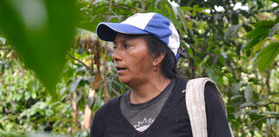 Eine ecuadoriansiche Kleinbäuerin trägt eine Schirmmütze, während sie mitten imRegenwald steht, über ihre linke Schulter gehängt trägt sie eine Tasche aus Stoff.