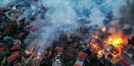 Das Bild zeigt eine Luftaufnahme eines Stadtviertels, Rauch und brennende Feuer