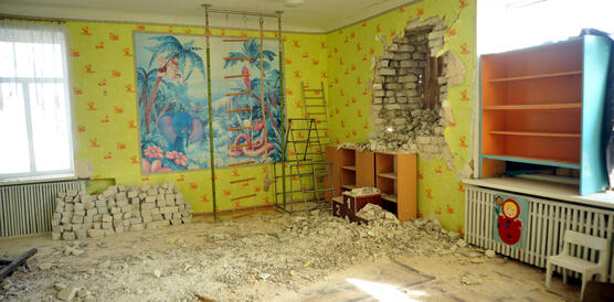 Das Bild zeigt einen Raum mit bunten Plakaten an der Wand und Kindermöbeln, es liegen Mauersteine verteilt auf dem Boden