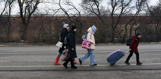 Das Bild zeigt mehrere Frauen und Kind, die mit Koffern eine Straße entlang gehen