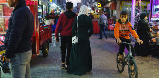 Auf einer türkischen Straße laufen ein Mann und eine Frau, sie trägt Kopftuch, neben ihnen fährt ein Kind auf einem Fahrrad.