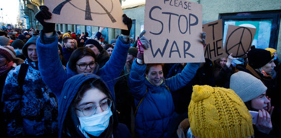 Das Bild zeigt mehrere Menschen mit Plakaten in der Hand, darauf zu lesen "Stop War"