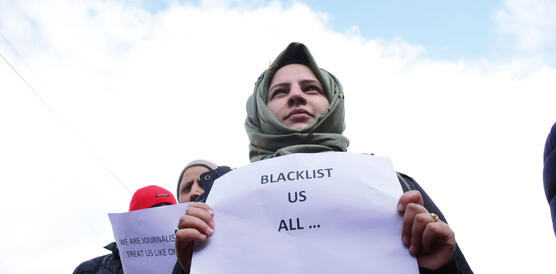 DemonstrantInnen, eine junge Frau mit Kopftuch steht für Pressefreiheit ein, sie hält ein Schilder hoch, dort steht: "Blacklist us all..."