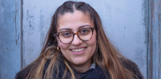 Eine junge Frau mit schulterlangem Haar trägt eine Hornbrille und lächelt.