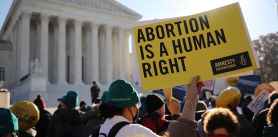 Das Bild zeigt eine Menge an Demonstrierenden vor einem Gebäude. Eine Person hält ein Amnesty-Schild mit der Aufschrift: "Abortion is a human right".