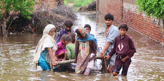 Männer, Frauen und Kinder waten durch ein Hochwasser.