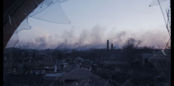 Blick durch ein zerbrochenes Fenster, in der ferne Rauch über einer Stadt