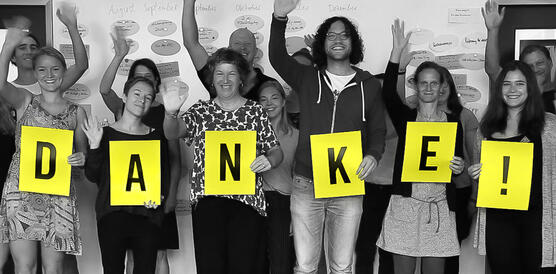 Das Bild zeigt ein Gruppenfoto mit vielen Personen, sie halten Schilder mit Buchstaben, die das Wort "Danke" ergeben.