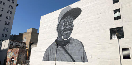 Ein Wandgemälde auf einer gestrichenen Backsteinwand stellt einen schwarzen Mann dar, der lächelt und eine Baseball-Kappe trägt.