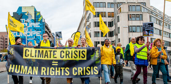 Das Bild zeigt mehrere Menschen auf der Straße, wie sie demonstrieren und gelbe Amnesty-Banner und Fahnen in der Hand halten