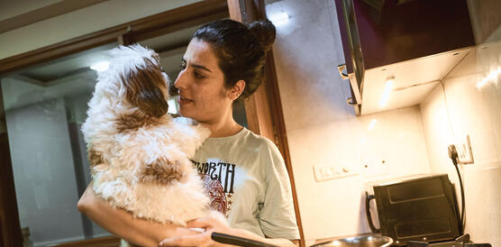 Eine junge indische Frau hält einen kleinen Hund in einer Küche auf ihrem Arm.