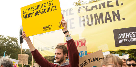 Das Bild zeigt mehrere Menschen mit Schildern in der Hand, darauf steht zum Beispiel "Klimaschutz ist Menschenrechtsschutz"