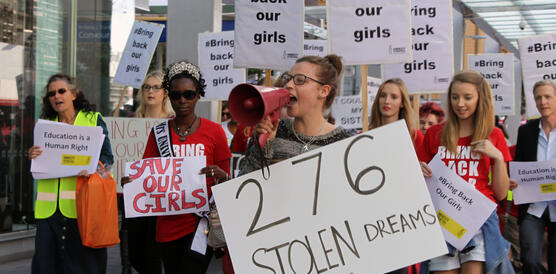 Das Foto zeigt eine größere Gruppen von Personen, die durch die Straße ziehen und Plakate hochhalten mit der Aufschrift "Bring back our girls". An der Spitze der Gruppe läuft eine Frau mit Megafon und einem Plakat, auf dem steht: "276 stolen dreams".