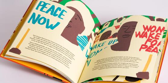 Ein aufgeschlagenes Buch auf einem Tisch, Kinderzeichnungen und die Worte "Peace Now" auf den Seiten.