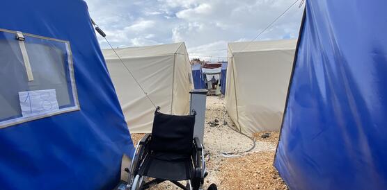 Das Bild zeigt einen Rollstuhl zwischen Zelten
