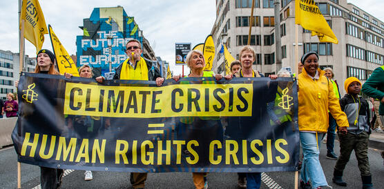 In gelb gekleidete Demonstrierende halten ein Banner mit der Aufschrift: "Climate Crisis = Human Rights Crisis"