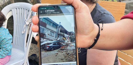 Ein Foto auf einem Handy, das ein zerstörtes Haus und ein von Trümmern verschüttetes Auto zeigt.