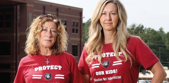 Zwei mittelalte Frauenstehen nebeneinander, beide schulterlanges Haar und das gleiche T-Shirt: "Protect our kids!", steht auf denen.