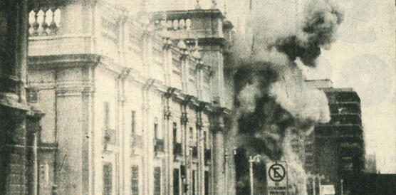 Das Forto zeigt ein großes Gebäude, das durch eine Explosion beschädigt wird. Rauch steigt auf.