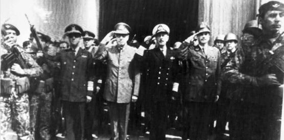 Das Foto zeigt vier Generäle, die nebeneinander stehen und salutieren. Sie sind umgeben von mit Gewehren bewaffneten Soldaten, die die Umgebung sondieren.