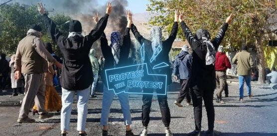   Vier Frauen stehen mit dem Rücken zur Kamera auf einer Straße. Sie heben ihre Hände in die Luft und zeigen mit beiden Händen das Victory-Zeichen. Weitere Menschen demonstrieren auf der Straße. Im Hintergund steigt Rauch auf.