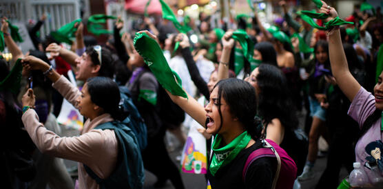 Das Foto zeigt eine große Menschenmenge, fast ausschließlich Frauen, die rufend und Tücher schwenkend durch die Straßen zieht.