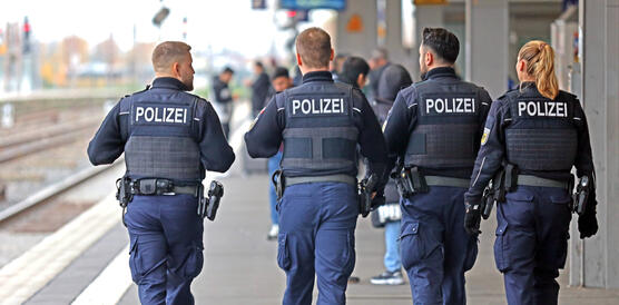 Das Bild zeigt vier Personen in Polizei-Uniformen von hinten fotografiert auf einem Bahnsteig-