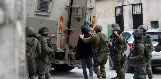 Das Bild zeigt mehrere Soldaten, ein Soldat führt einen Mann in einen Einsatzwagen