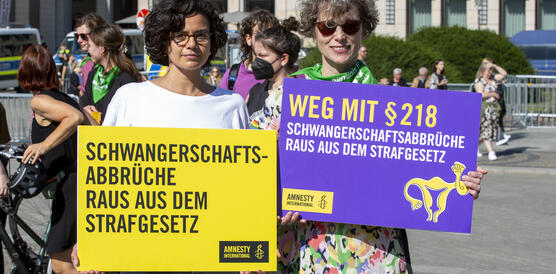 Das Foto zeigt zwei Demonstrantinnen, die Schilder hochhalten, auf denen unter anderem steht "Weg mit Paragraf 218".