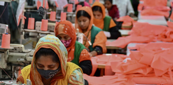 Eine Reihe von Frauen an Nähmaschinen, an ihrer Seite rote Stoffe.
