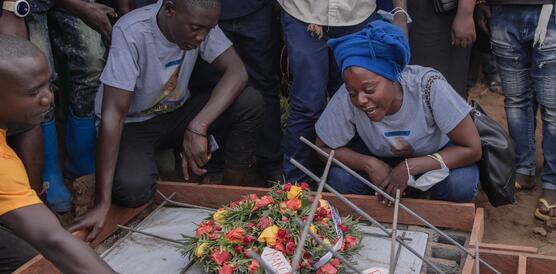 Trauernde Menschen an einem Grab, in der Mitte ein großer Blumenstrauß.