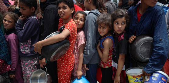 Kinder stehen eng gedrängt in einer Schlange, sie haben Töpfe in der Hand