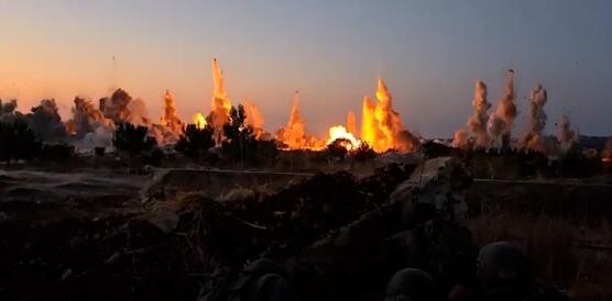Das Foto zeigt mehrere Gebäude, die durch Explosionen zerstört werden. Flammen und Rauch und Geröll steigen meterhoch in die Luft.