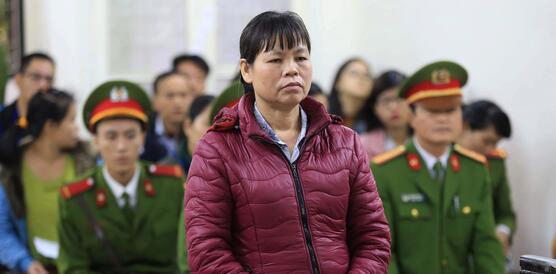 Das Foto zeigt  Cấn Thị Thêu stehend in einem Gerichtssaal. Sie hat die Hände gefaltet und Blick nach vorne. Hinter ihr sitzen Beamte in Uniform und Publikum.