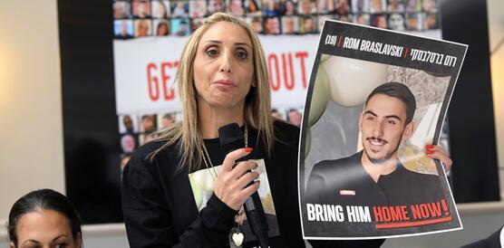 Eine Frau mit einem Mikrofon und einem Plakat, darauf zu sehen ein junge Mann und der Name Rom Braslavski